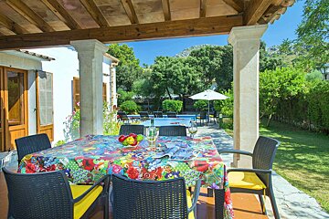 A table with a colorful table cloth sits under a pergola