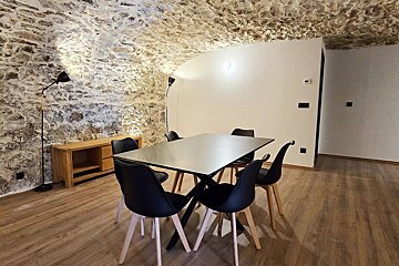 A rustic-modern dining room with a stone-vaulted ceiling, wooden floor, black dining table and chairs, and a sleek wooden sideboard.