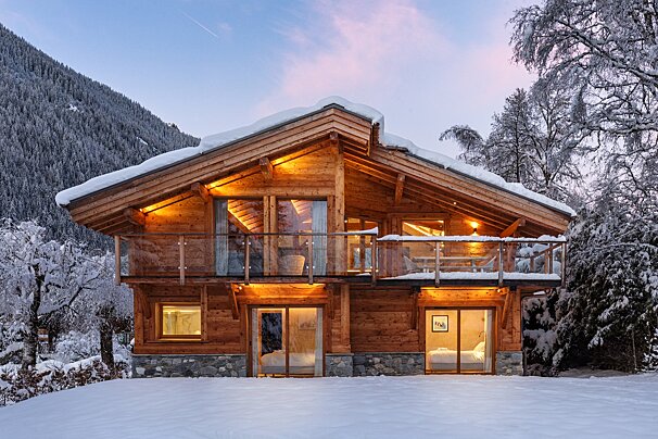 A large wooden house is surrounded by snow and trees