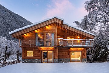 A large wooden house is surrounded by snow and trees