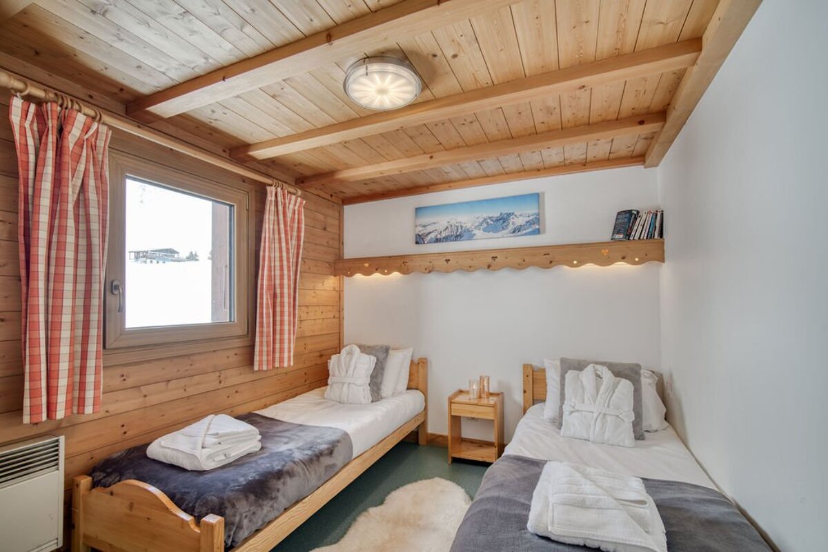 Cozy twin bedroom with wood paneling, white walls, and a window showing a snowy landscape. Two single beds have white robes and towels.