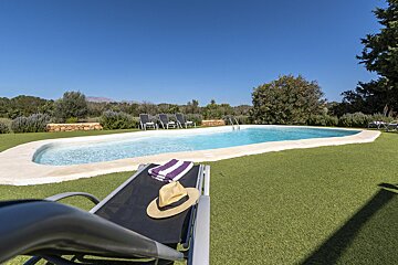 A lawn chair with a hat and striped towel sits next to a large swimming pool