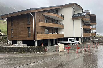 A modern multi-story building with wood and white siding and balconies, currently under construction on a rainy day, with a white truck parked below.