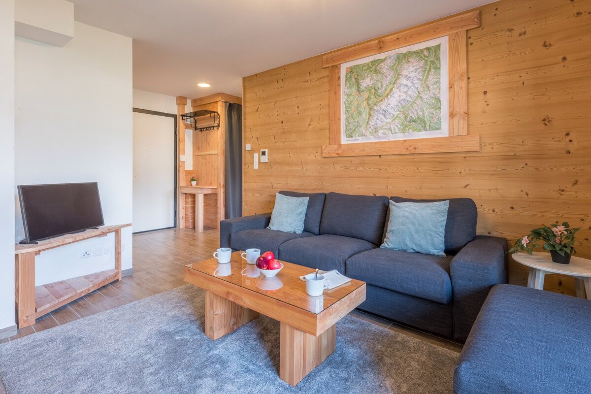 Cozy, wood-paneled living room with a gray sofa, wooden coffee table, TV on a stand, and a map picture above the sofa.