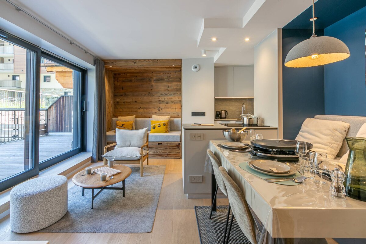 Cozy modern apartment featuring a set dining table, a light-filled living area, and a rustic wood-paneled seating nook.