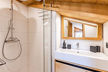 Cozy rustic bathroom featuring a glass shower, white sink, and an illuminated mirror under a sloped wooden ceiling.