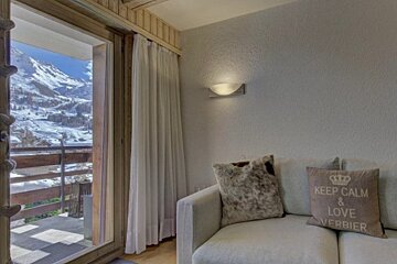 Cozy living room with a sofa next to a glass door that opens to a balcony with stunning snowy mountain views.