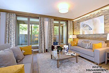A modern living room featuring two grey sofas with yellow pillows, a coffee table, large windows, and a stone accent wall with a polar bear artwork.