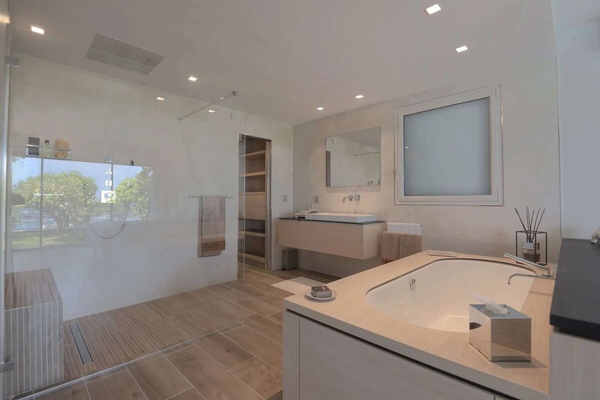 A modern, light-toned bathroom with a glass walk-in shower, a built-in bathtub, a floating vanity, and light wood-look flooring and accents.