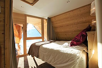Cozy wood-paneled cabin bedroom with a sunlit bed and windows overlooking snowy mountains.