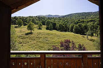 A balcony overlooking a lush green field with trees and mountains in the background