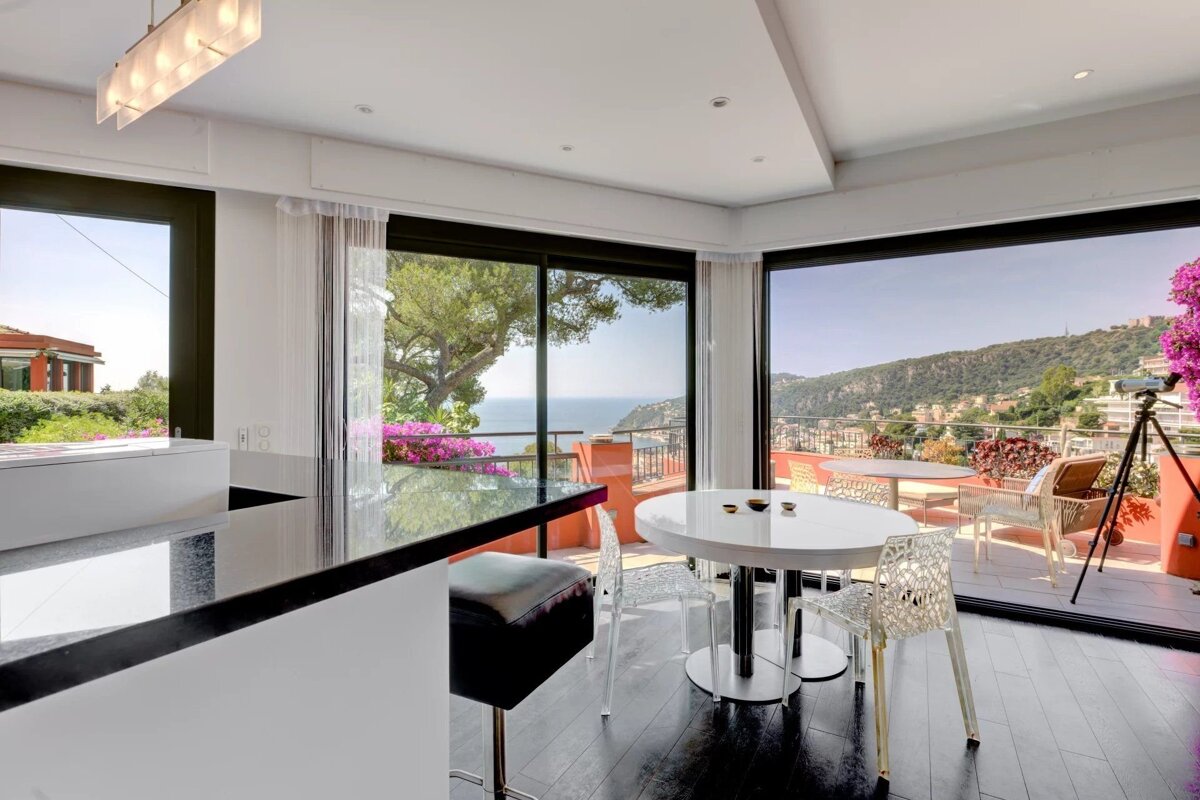 Modern kitchen and dining room with large floor-to-ceiling windows overlooking a beautiful coastal hillside view.
