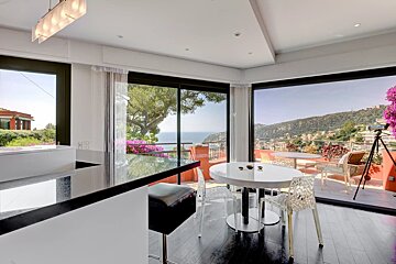 Modern kitchen and dining room with large floor-to-ceiling windows overlooking a beautiful coastal hillside view.