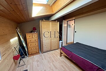 Cozy wooden attic bedroom featuring a bed, wardrobe, chest of drawers, and a slanted ceiling with a bright skylight.