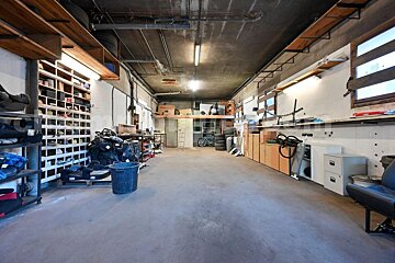 A spacious, well-lit garage or workshop with concrete floors, extensive wall shelving, various stored items, and a loft area at the back.