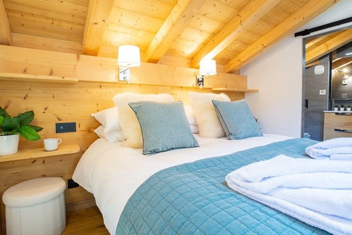 Cozy wooden cabin-style bedroom featuring a bed with blue and white bedding under a slanted timber ceiling.