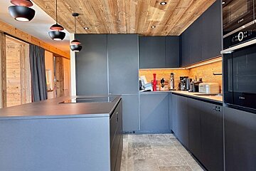 Modern kitchen with sleek dark gray cabinets, a wooden ceiling, a large island, and contemporary pendant lights.