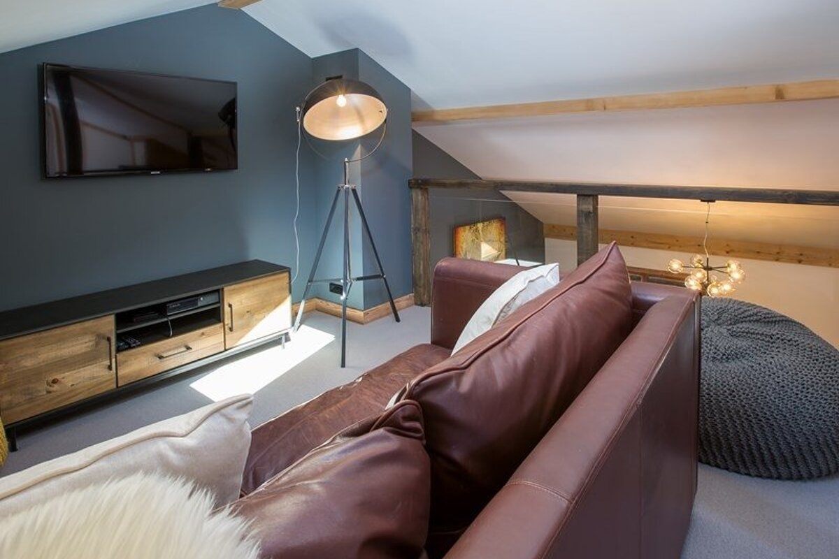 Modern loft living room featuring a brown leather couch, a TV on a blue wall, rustic wooden media console, and a tripod floor lamp.