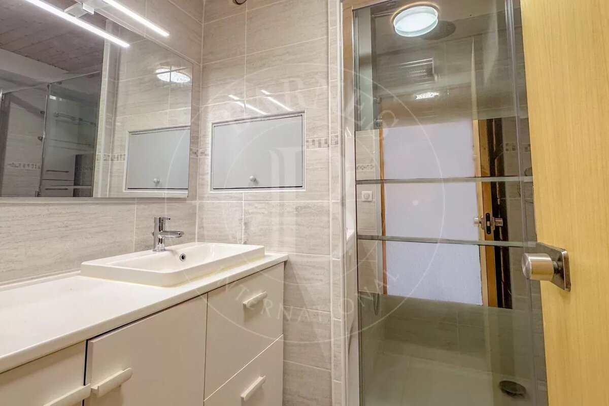 Modern bathroom featuring light grey tiles, a white vanity with an integrated sink, a large mirror, and a glass-enclosed shower.