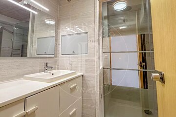 Modern bathroom featuring light grey tiles, a white vanity with an integrated sink, a large mirror, and a glass-enclosed shower.