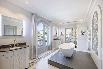 An elegant, spacious bathroom features a freestanding tub on a raised platform, arched balcony doors, stylish vanities, and decorative floor and wall accents.