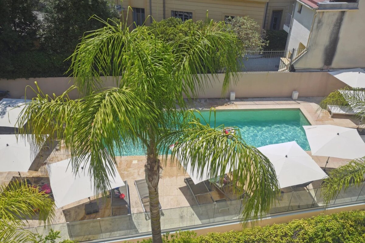 An overhead view of a backyard swimming pool surrounded by lounge chairs, white umbrellas, and a palm tree.