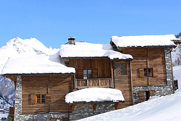 A wooden house with snow on the roof and a mountain in the background
