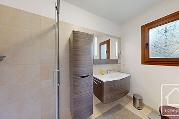 Modern bathroom featuring a glass shower, sleek wood-tone vanity with a mirror and lights, tall storage cabinet, and a textured window.