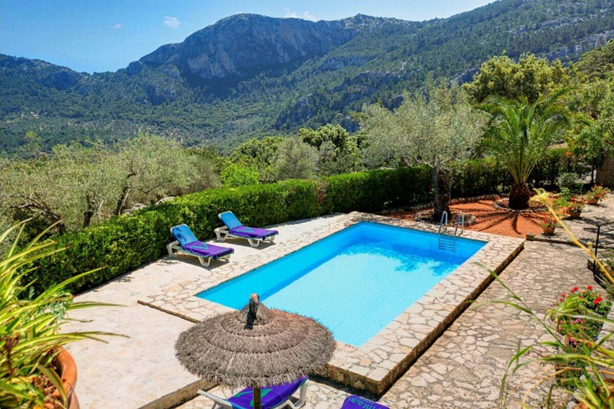 A swimming pool surrounded by chairs and umbrellas with mountains in the background