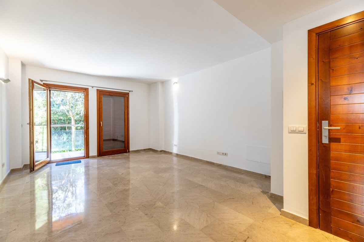 Bright, empty room with white walls, shiny marble floor, and wooden-framed doors/windows, one open to a green outdoor view.