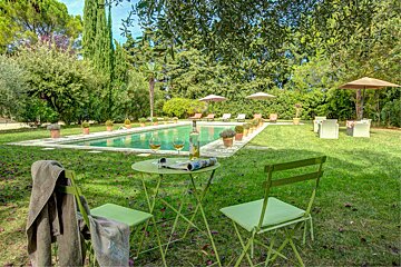 A bottle of wine sits on a table in front of a swimming pool