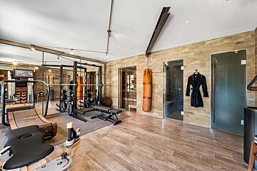 A luxurious home gym featuring modern fitness equipment, a leather punching bag, and integrated sauna and steam shower rooms, all with wood finishes.