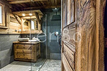 Cozy rustic bathroom in a chalet, featuring a wooden vanity, stone sink, slate shower tiles, and a textured wooden door.