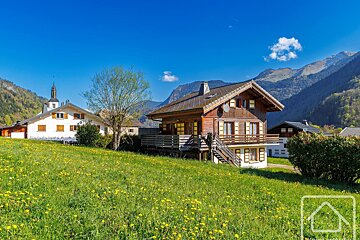A house sits in the middle of a grassy field with mountains in the background