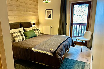 A cozy, modern bedroom with a wooden feature wall, bed, and a door opening to a snowy winter view from a balcony.