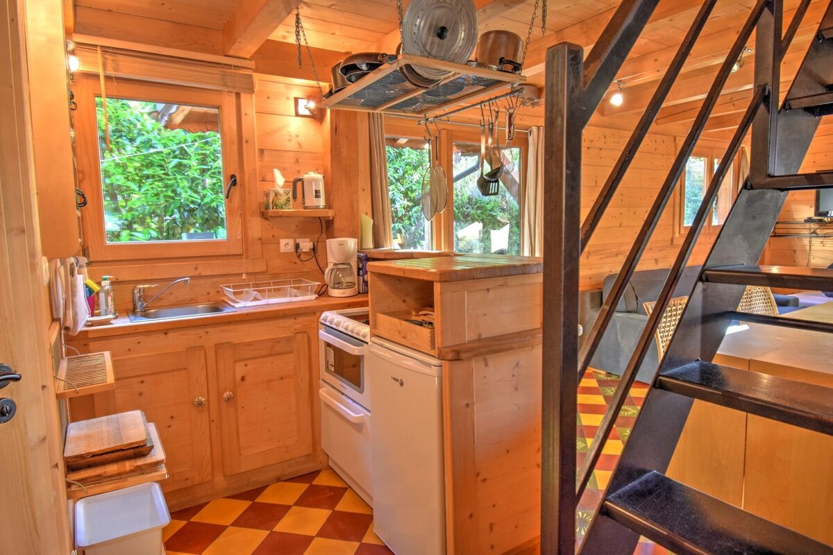 Cozy, rustic cabin kitchen with warm wood paneling, checkerboard tiles, a small stove, and a metal staircase in the foreground.