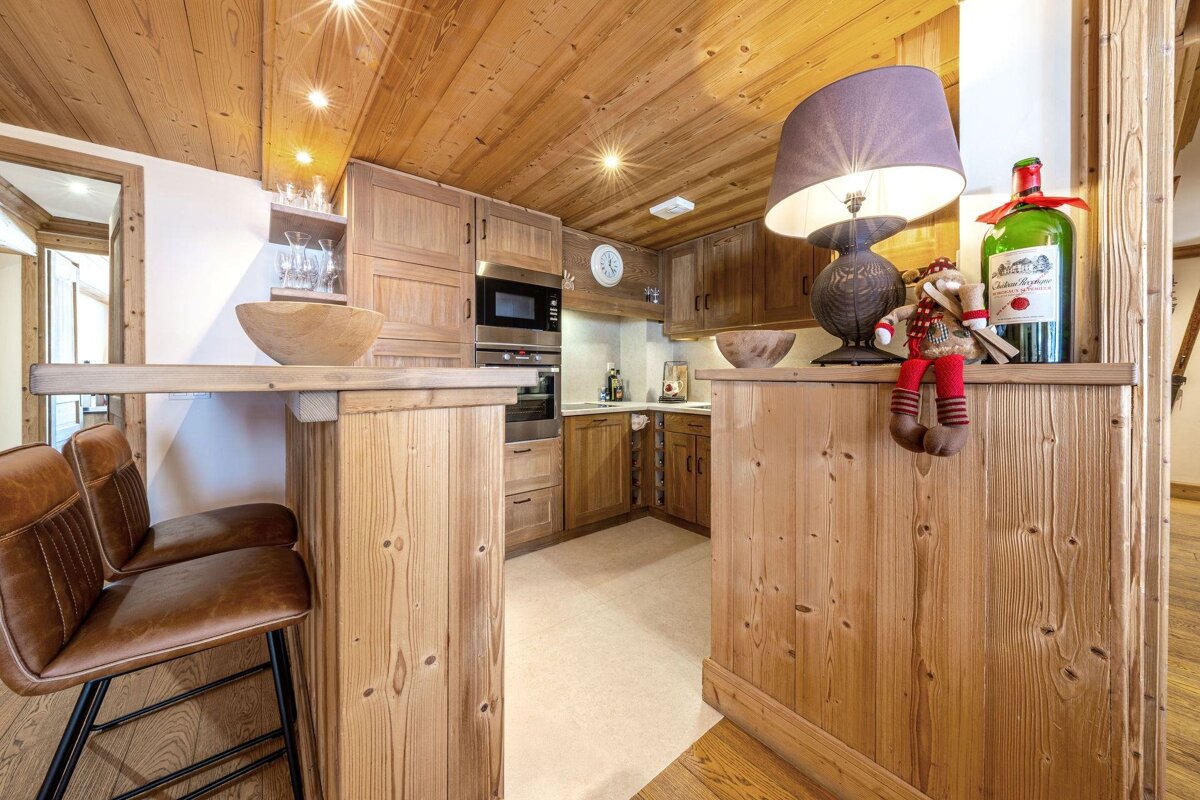 A warm, rustic chalet kitchen featuring extensive natural wood cabinetry, a breakfast bar with woven stools, and modern appliances. Cozy and inviting.