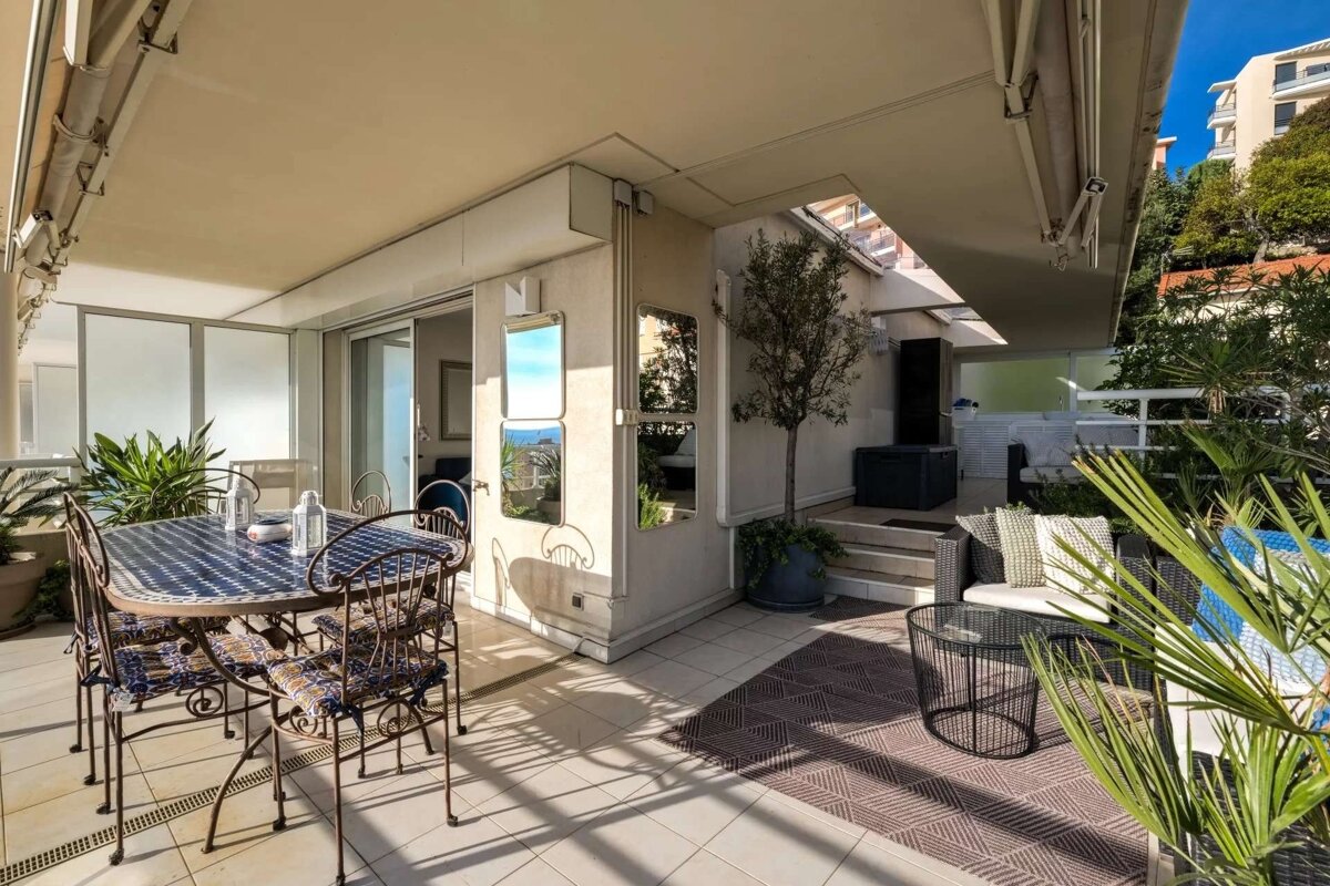 A sunlit outdoor terrace with a dining set, seating area, and potted plants. Mirrors reflect the bright sky, creating an open, airy feel.