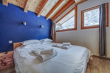 A bedroom with a blue wall and two windows