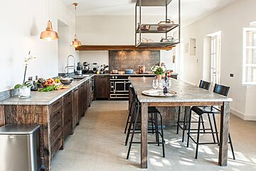 A kitchen with a long wooden table and stools