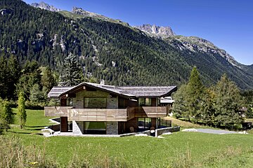 A house in the middle of a lush green field with mountains in the background