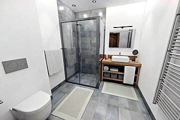 A contemporary bathroom with a glass shower, floating toilet, wooden vanity, vessel sink, and grey and white tile accents.