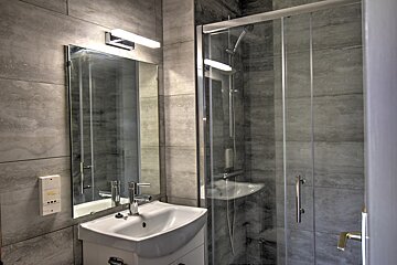 A modern bathroom with gray tiled walls, a white sink, an illuminated mirror, and a glass shower enclosure.