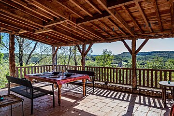 A table with a checkered tablecloth sits on a porch overlooking a forest