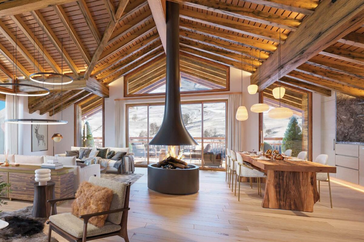 Cozy chalet interior with a vaulted wooden ceiling, central hanging fireplace, dining and living areas, and scenic mountain views.