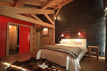 A cozy bedroom mixes rustic wood beams, a striking red sliding door, a dark tiled wall, a white bed, and a cowhide rug for a modern chalet feel.
