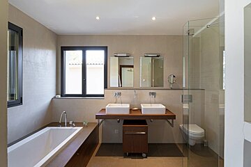 Modern neutral-toned bathroom with a bathtub, double vessel sinks, two mirrors, and a glass shower partition.