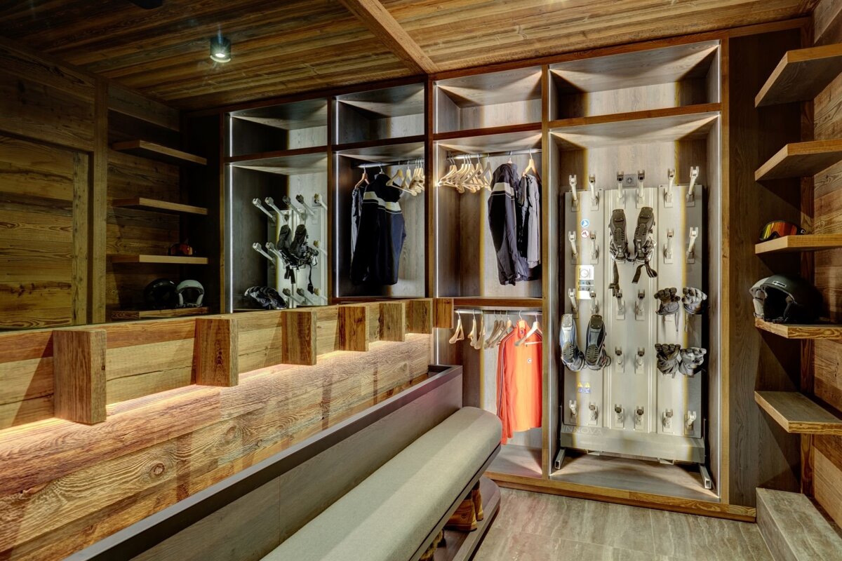 A luxurious, wood-paneled ski room with organized storage for boots, helmets, jackets, and a long bench for preparing for the slopes.