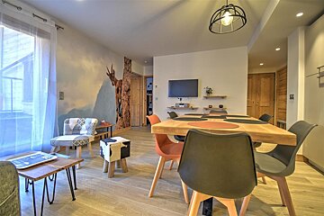 Modern dining and living area featuring a large wooden table with colorful chairs and a scenic wall mural of a mountain goat.