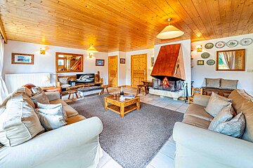 An inviting, rustic living room with a lit fireplace, warm wood ceiling, comfortable sofas, and a coffee table with champagne.
